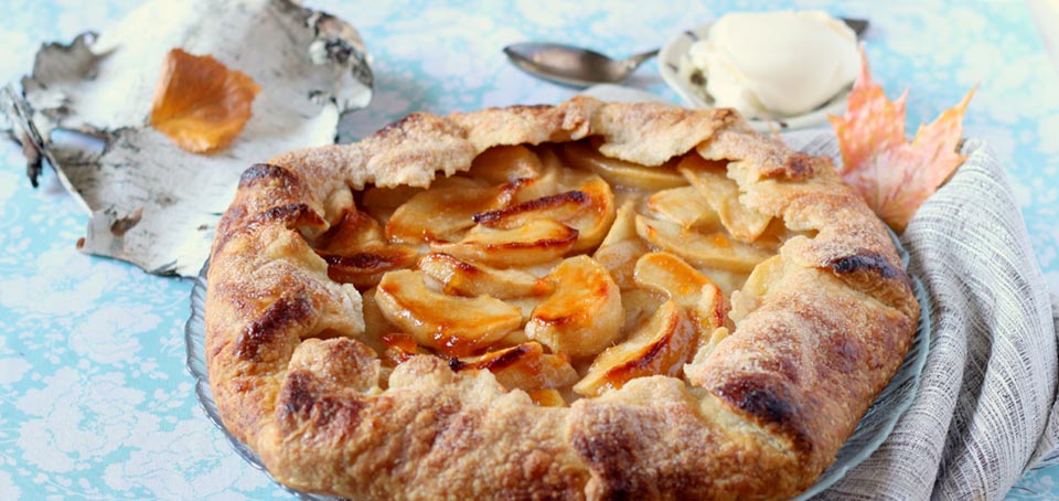 Close-up of a table-setting featuring a pie and autumn leaves.